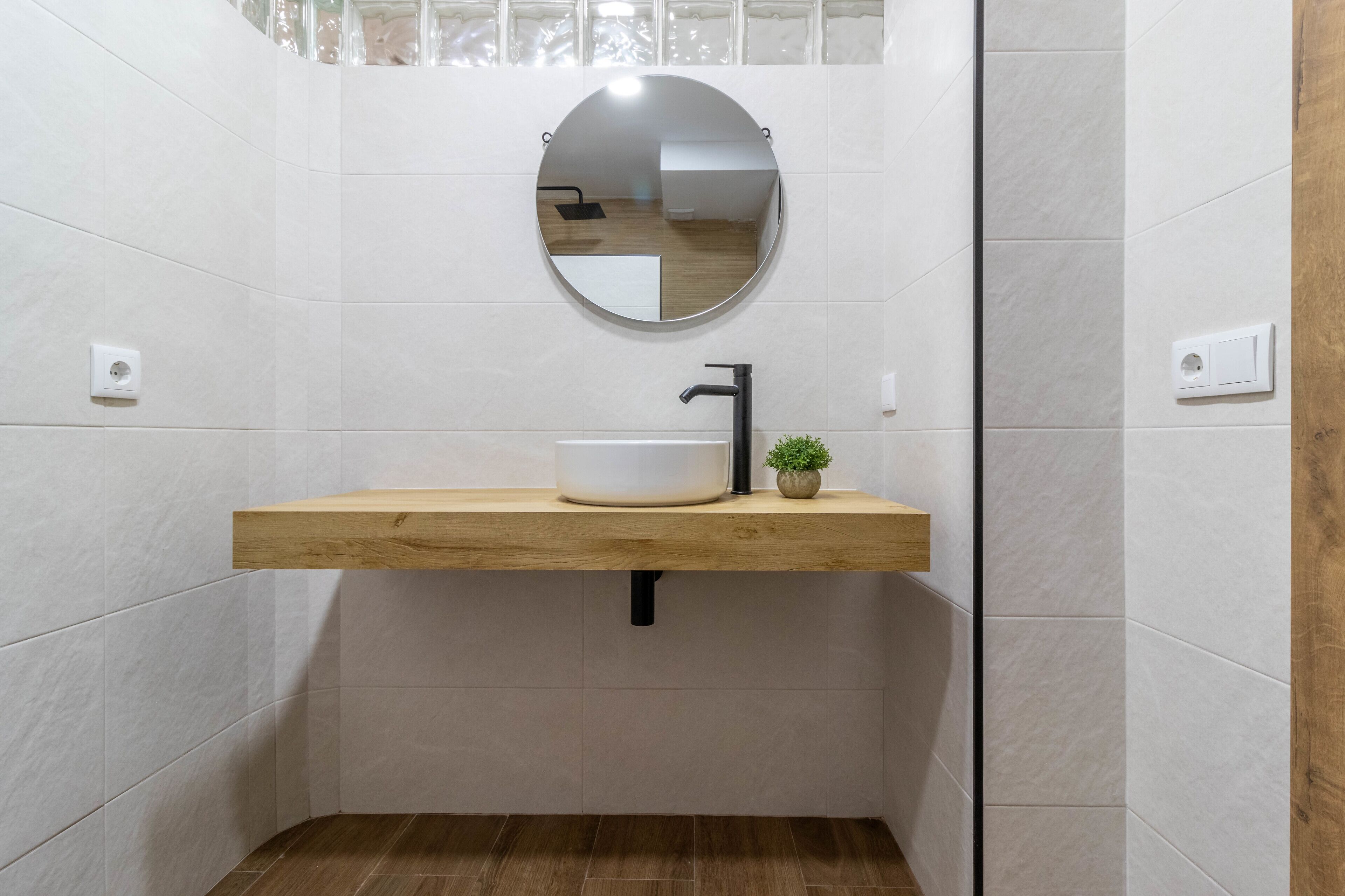 Un baño con tocador de madera, un espejo redondo y una pequeña planta en maceta.