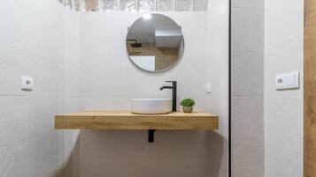 Un baño con tocador de madera, un espejo redondo y una pequeña planta en maceta.