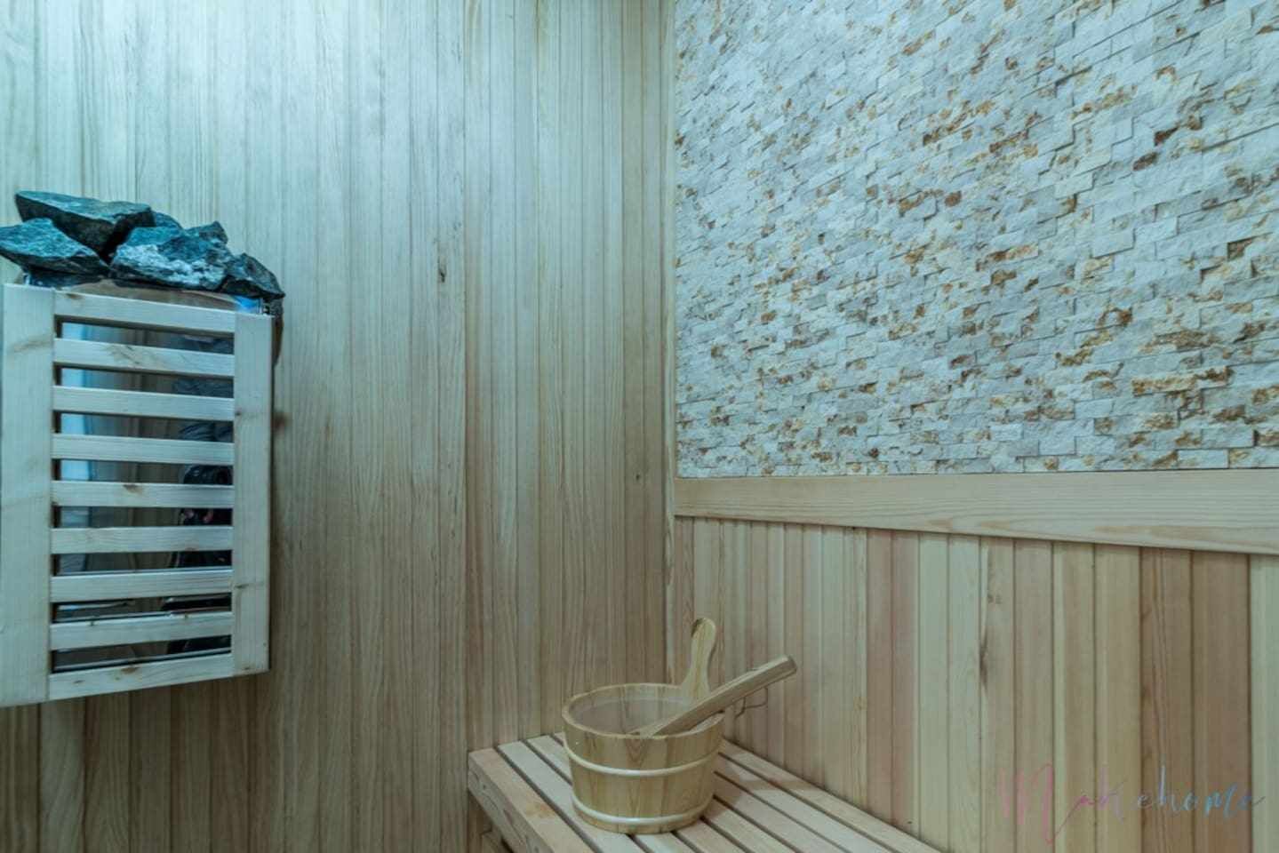 A wooden sauna room with a wooden bench, a wooden bucket, and a wooden shelf with rocks.