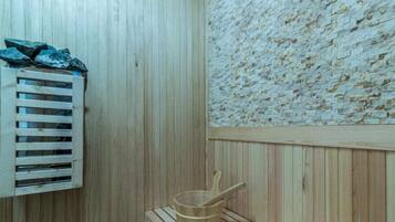 A wooden sauna room with a wooden bench, a wooden bucket, and a wooden shelf with rocks.