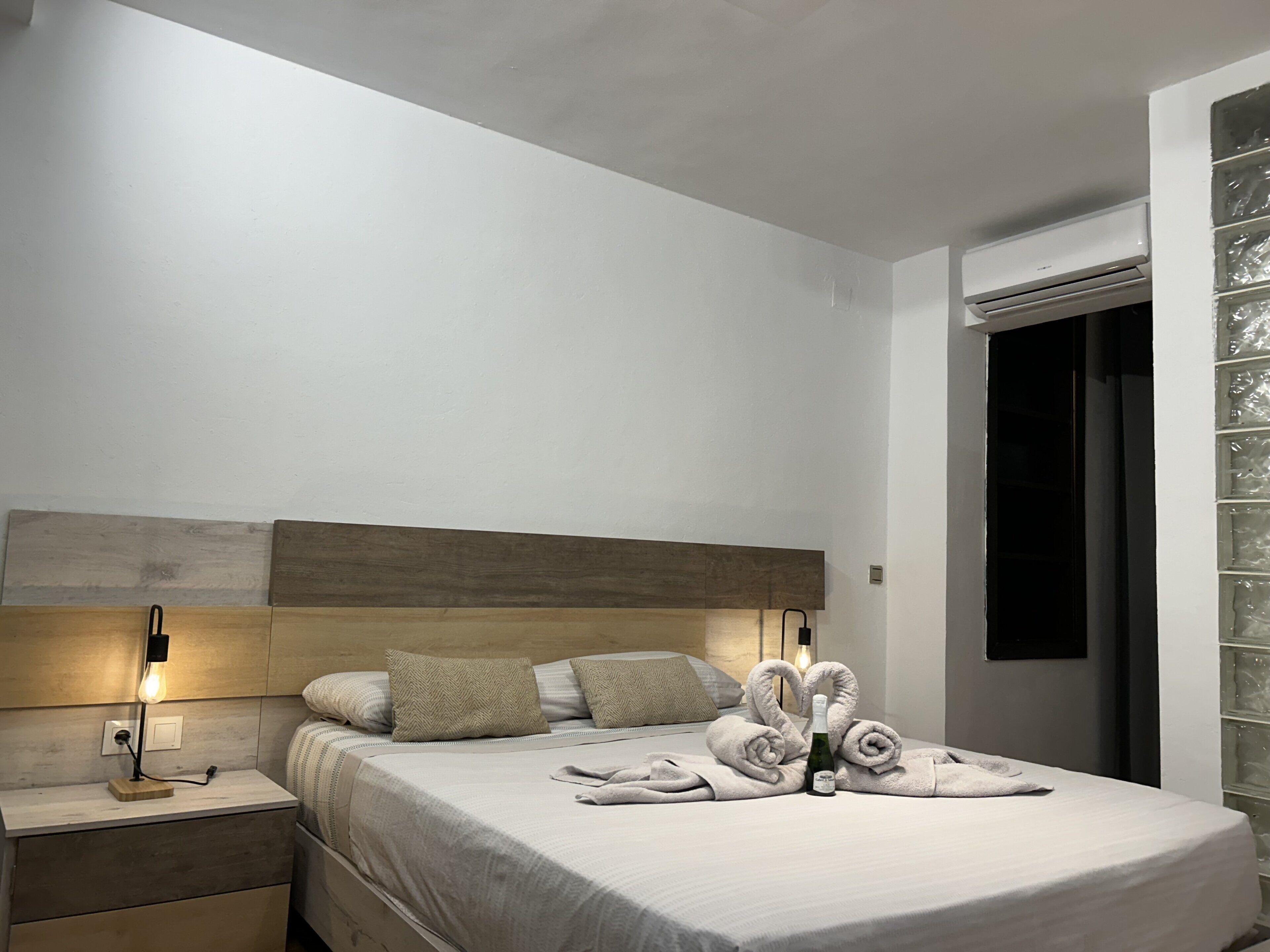 Une chambre d’hôtel moderne avec un lit, une lampe de chevet et une bouteille de vin.