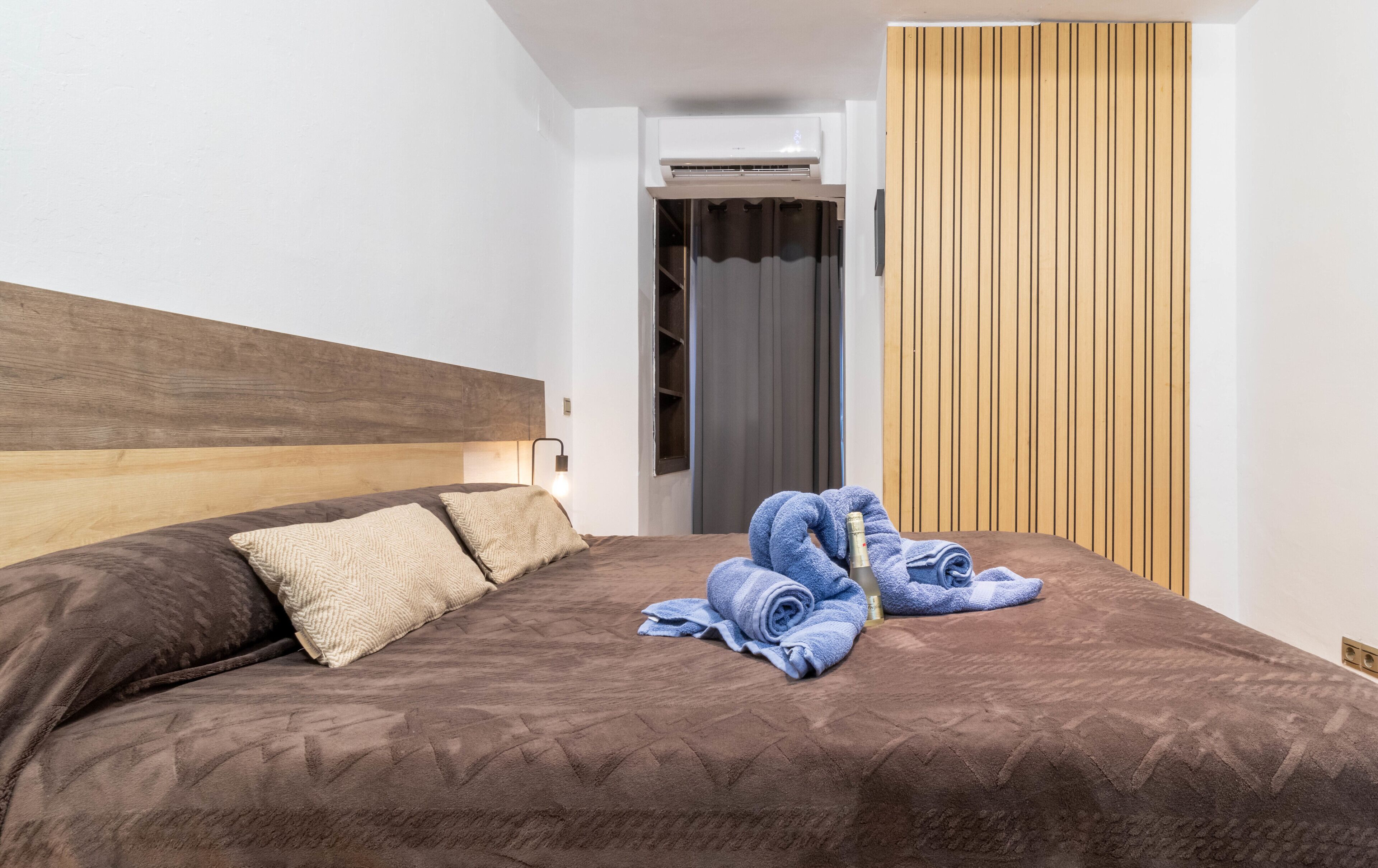 A hotel room with a wooden headboard, a bed with brown bedding, a blue towel, and a bottle of champagne.