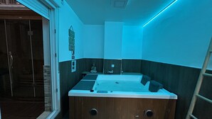 Un baño moderno con una bañera de madera, un lavamanos pequeño y un inodoro. Hay un perchero y un espejo en la pared.