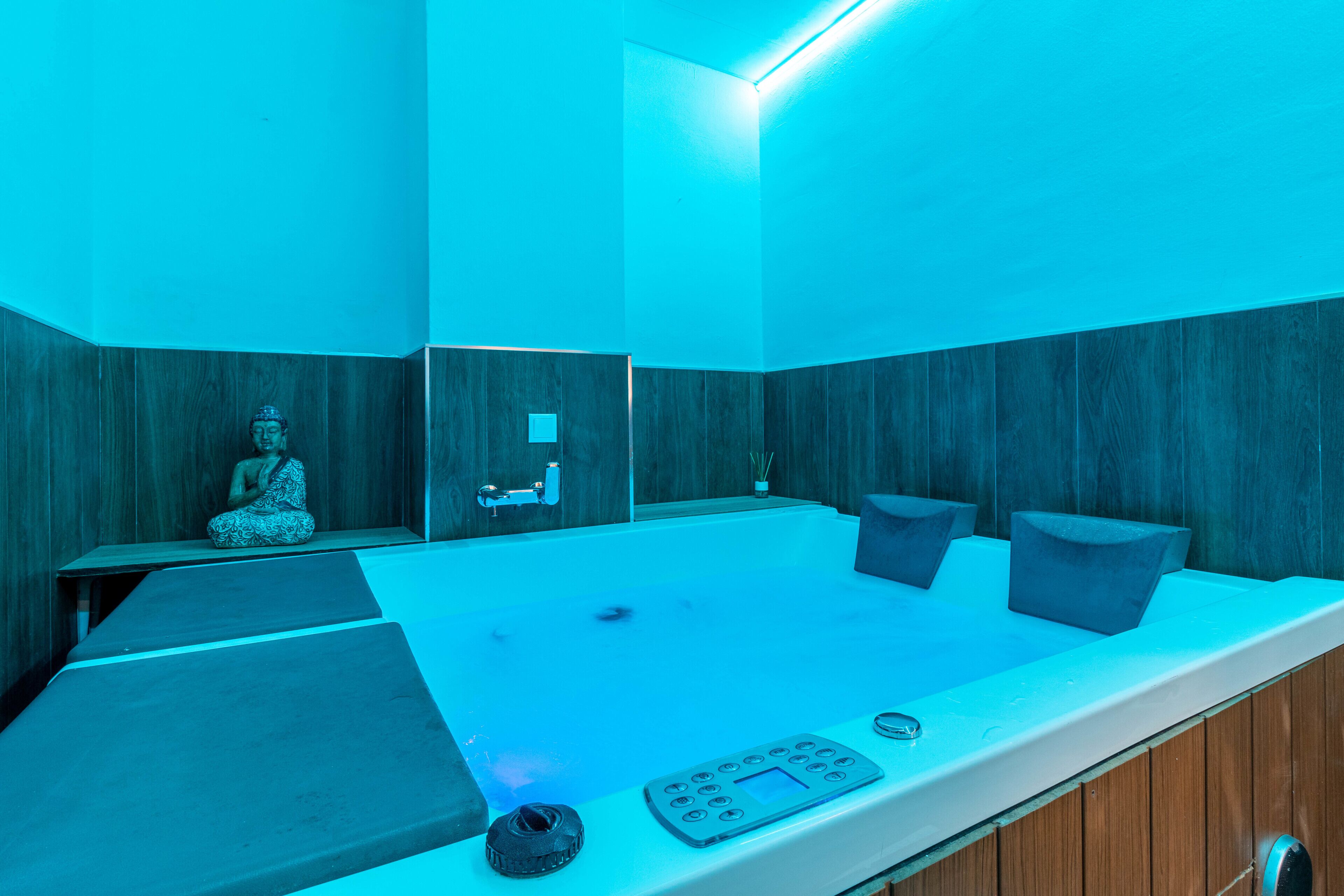 Un moderno cuarto de spa con un panel de pared de madera, una bañera grande y una estatua de Buda.