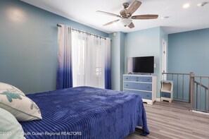A bedroom with a bed, a ceiling fan, a TV, and a dresser.