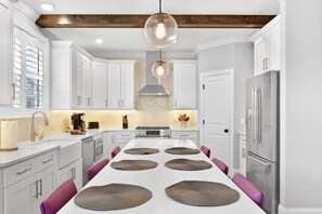Une cuisine moderne avec des meubles blancs, un îlot central agrémenté de sets de table, un réfrigérateur en acier inoxydable et un luminaire suspendu.