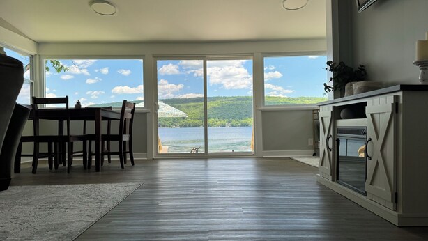 A spacious room with a large sliding glass door leading to a lake view, a dining area with a table and chairs, and a kitchenette with a stove.