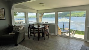A cozy living room with a dining area, large windows offering a view of a lake and hills, and a framed picture on the wall.