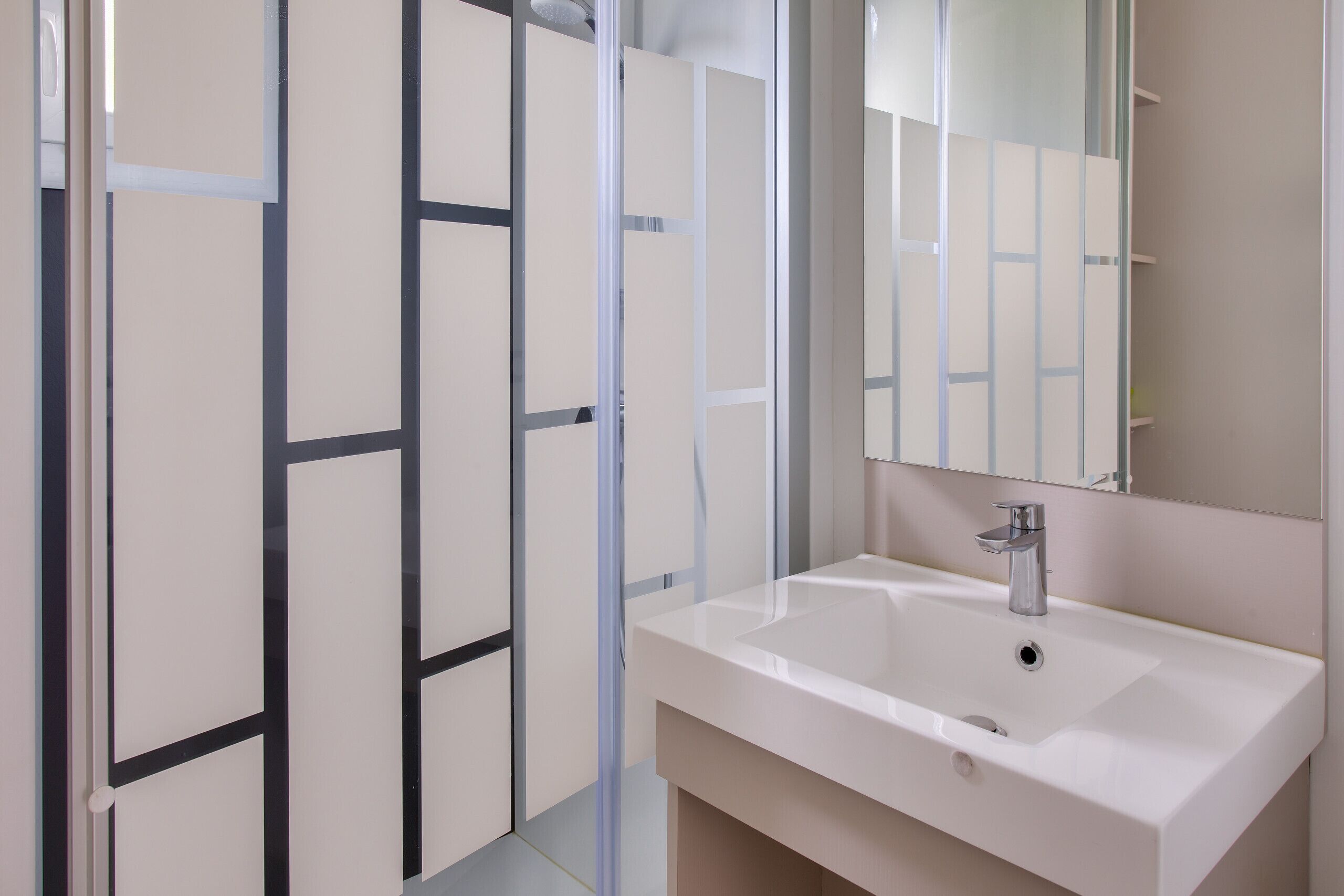 Une salle de bain moderne avec un lavabo blanc, un miroir et une cabine de douche en verre.