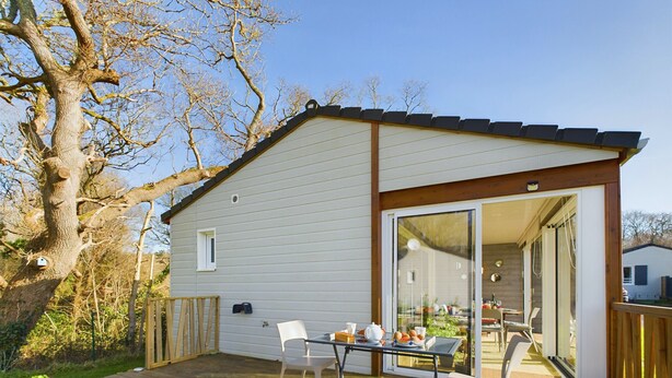 A single-story house with a deck, a sliding glass door leading to a patio, and a small window. - Chalet for 4, terrace & heated pool (Pont-l´Abbé)