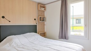 A neatly made bed in a room with a wooden headboard, a small wooden shelf with a 'LOVE' sign, and a window with a curtain. - Chalet for 4, terrace & heated pool (Pont-l´Abbé)
