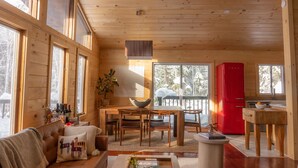 Ein gemütliches Blockhaus-Interieur mit Holzwänden, großen Fenstern, einer Essecke und einem roten Kühlschrank.