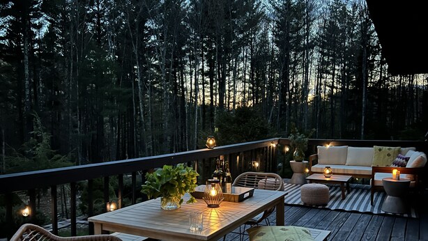 Eine Terrrasse im Freien mit einem Holztisch, Stühlen und einer Couch, umgeben von einem Wald.