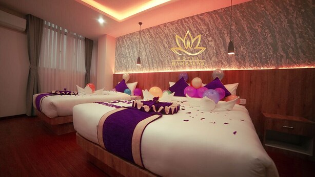 A hotel room with two beds, a wooden headboard, a wall with a lotus flower logo, and a ceiling light. - Hotel Namaskar (Kathmandu)