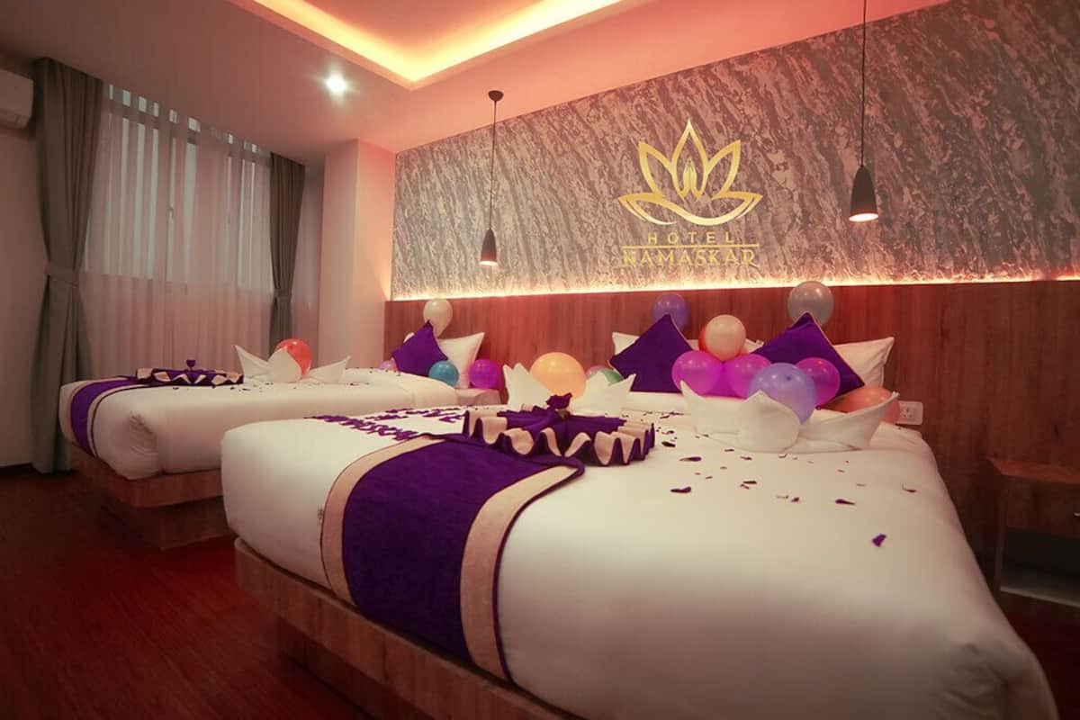 A hotel room with two beds, a wooden headboard, a wall with a lotus flower logo, and a ceiling light.