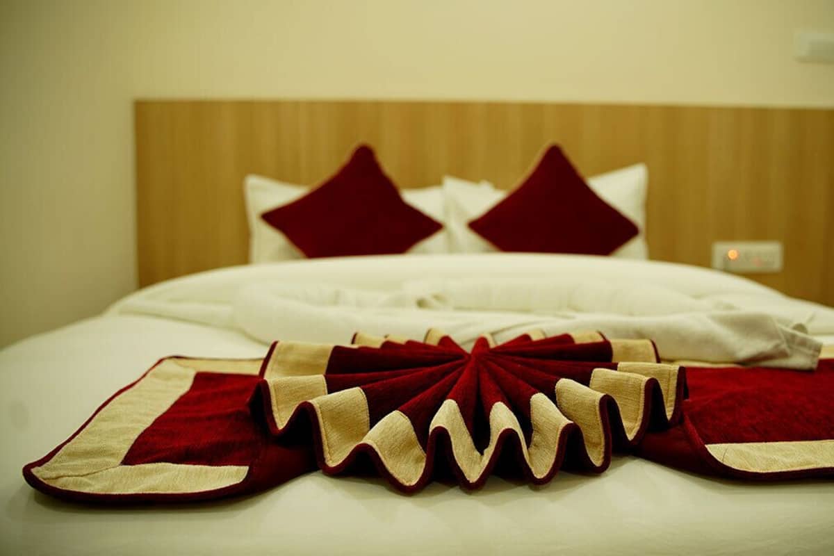 A neatly made bed with white linens, two red pillows, and a red and beige decorative pillow.