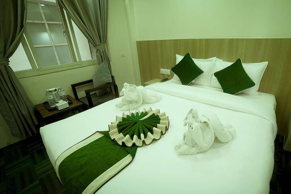 A hotel room with a neatly made bed, a bedside table with a lamp, and a window with curtains.