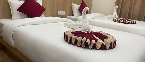 A hotel room with two beds, each with white bedding and maroon pillows. There is a decorative swan towel on the beds.