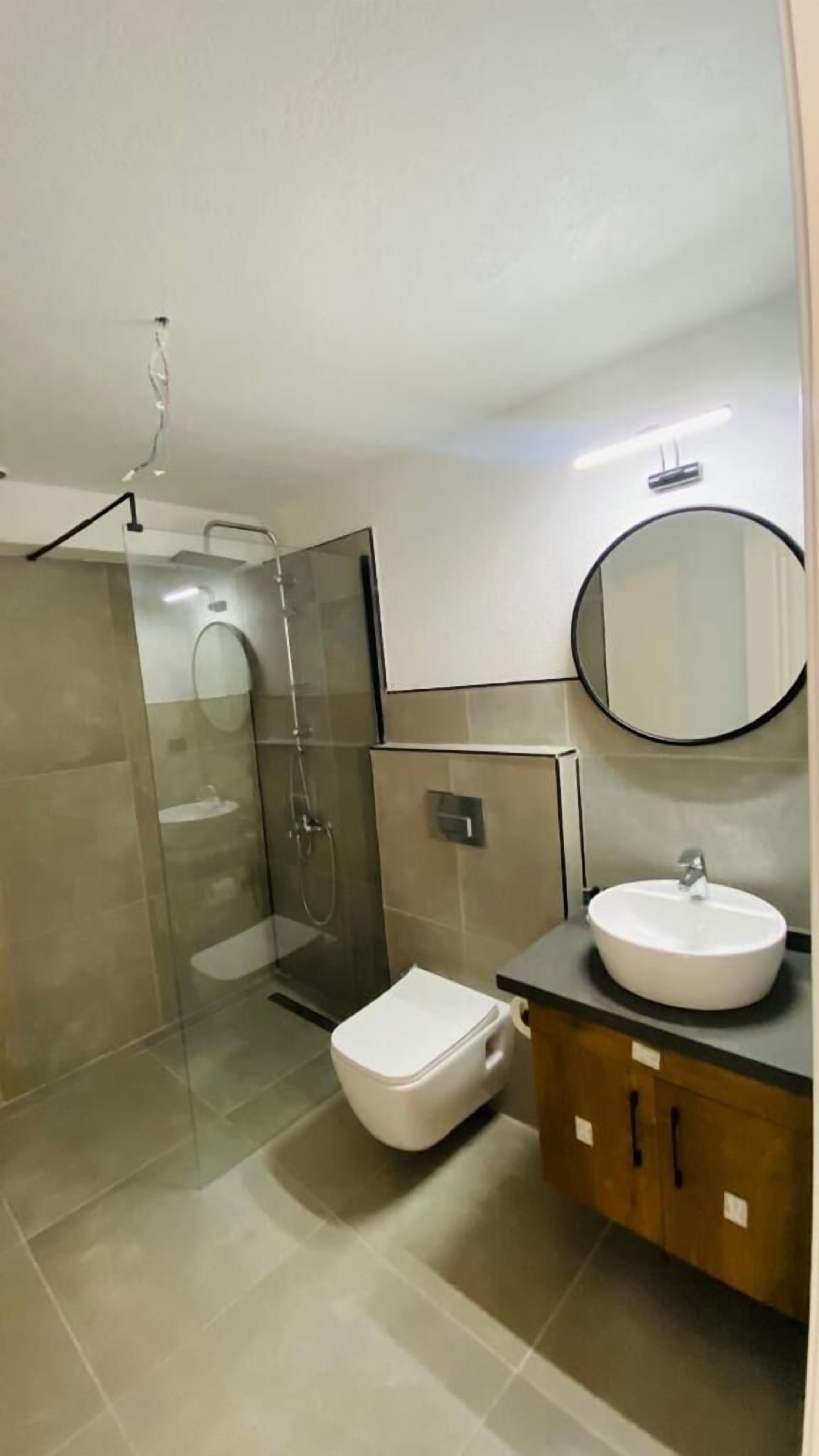 A modern bathroom with a glass-enclosed shower, a toilet, a sink with a mirror, and a vanity with cabinets.