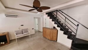 Ein modernes Wohnzimmer mit einer Couch, einem Holzkabinett, einem Deckenventilator und einer Treppe.