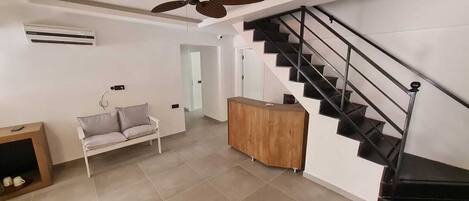 Una sala de estar moderna con un sofá, un mueble de madera, un ventilador de techo y una escalera.