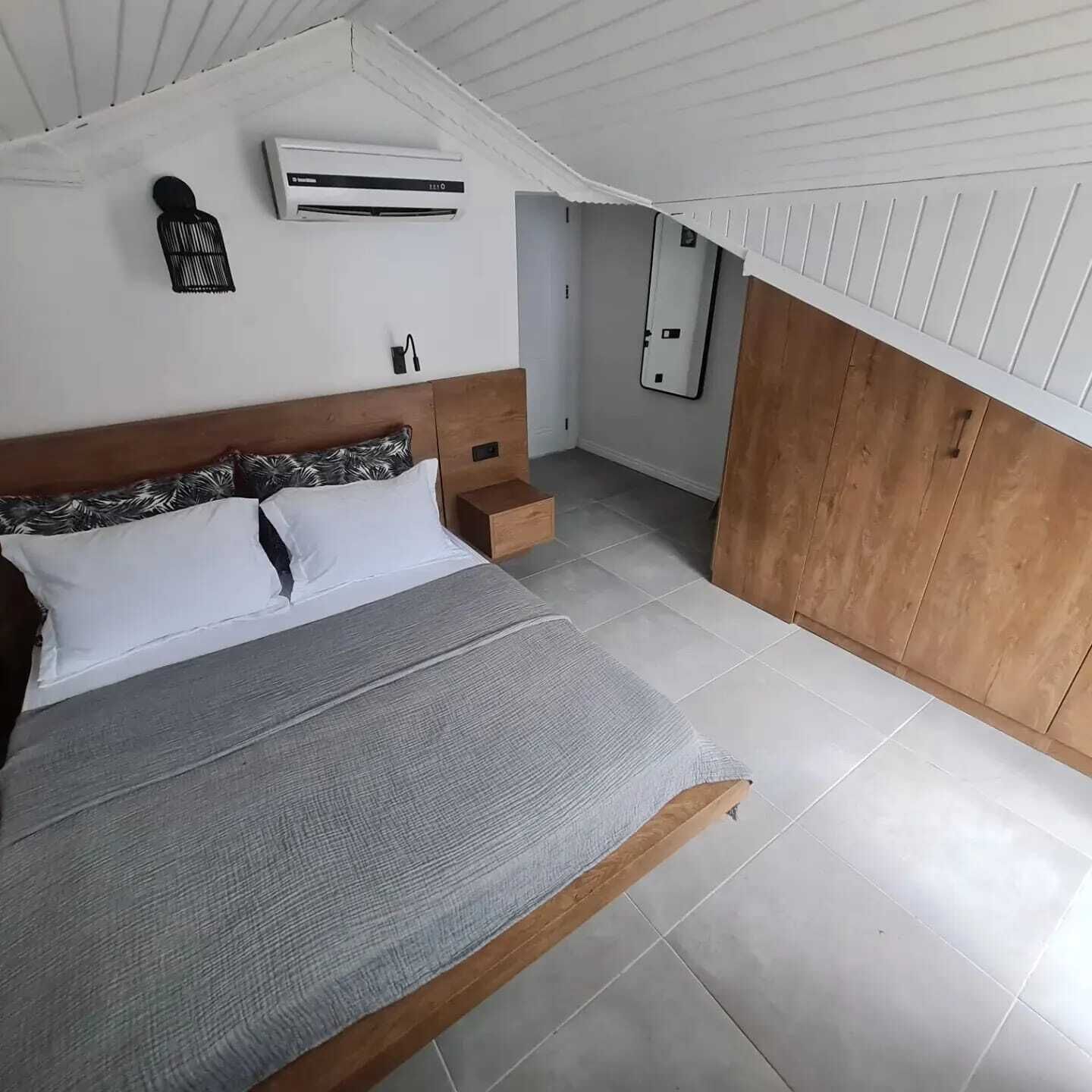 A bedroom with a bed, a nightstand, an air conditioning unit, and a wooden panel wall.