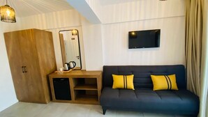 Ein modernes Zimmer mit einer dunkelgrauen Couch, einem Holzschrank, einem kleinen Tisch mit Spiegel und einem an der Wand befestigten Fernseher.