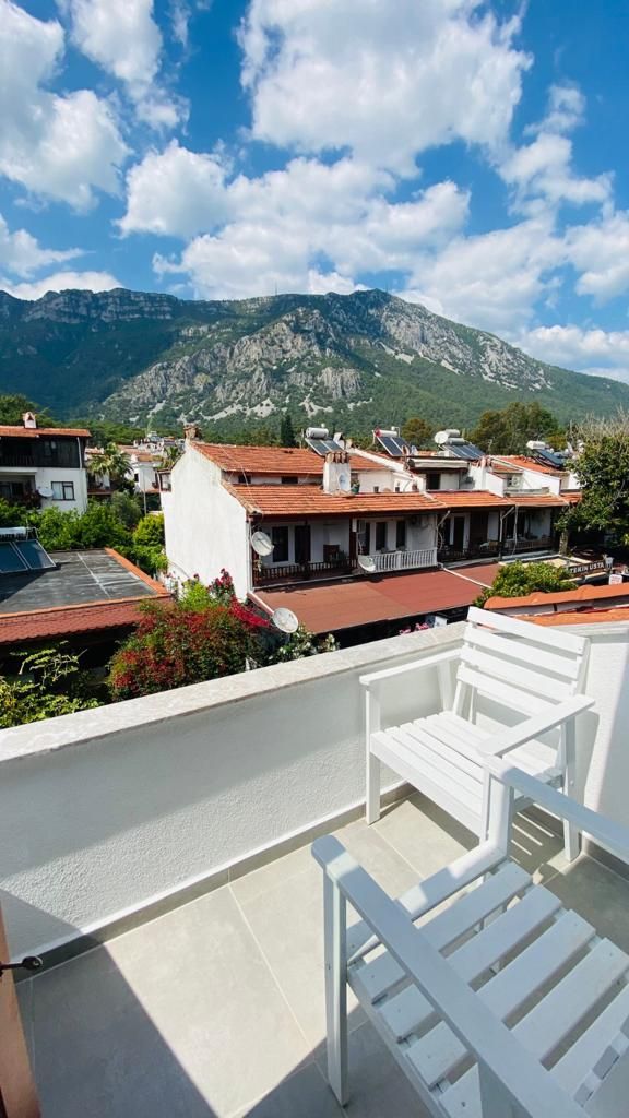 Un balcón con muebles blancos, con vistas a un paisaje montañoso y edificios al fondo.