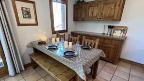 A dining table set with plates, glasses, and candles, in a kitchen with wooden cabinets and a window. - Les Granges 13, 6-8 person 50m from the slopes (Plagne Montalbert)