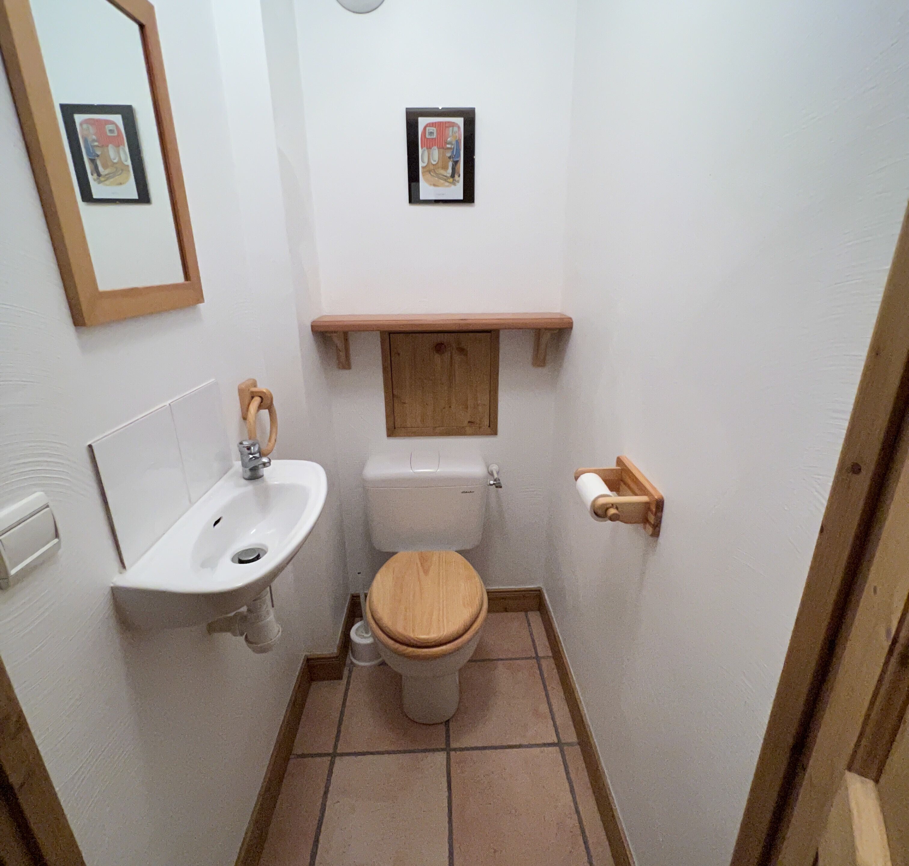 Une petite salle de bain avec un lavabo blanc, des toilettes en bois et une étagère en bois au-dessus des toilettes.