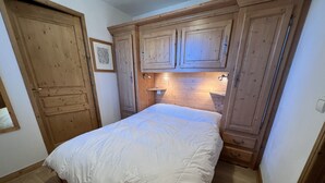 A bedroom with a bed, wooden wardrobe, and a small bedside table with a lamp. - Les Granges 13, 6-8 person 50m from the slopes (Plagne Montalbert)