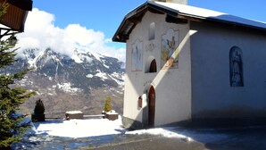 A church with a bell tower, snow-covered ground, and a mountain in the background.