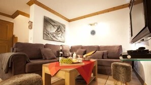 A living room with a brown sofa, a wooden coffee table with a red tablecloth, a television, and a painting on the wall.