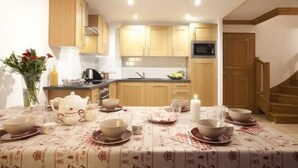 A cozy kitchen with wooden cabinets, a dining table set for tea, and a staircase leading to another level.