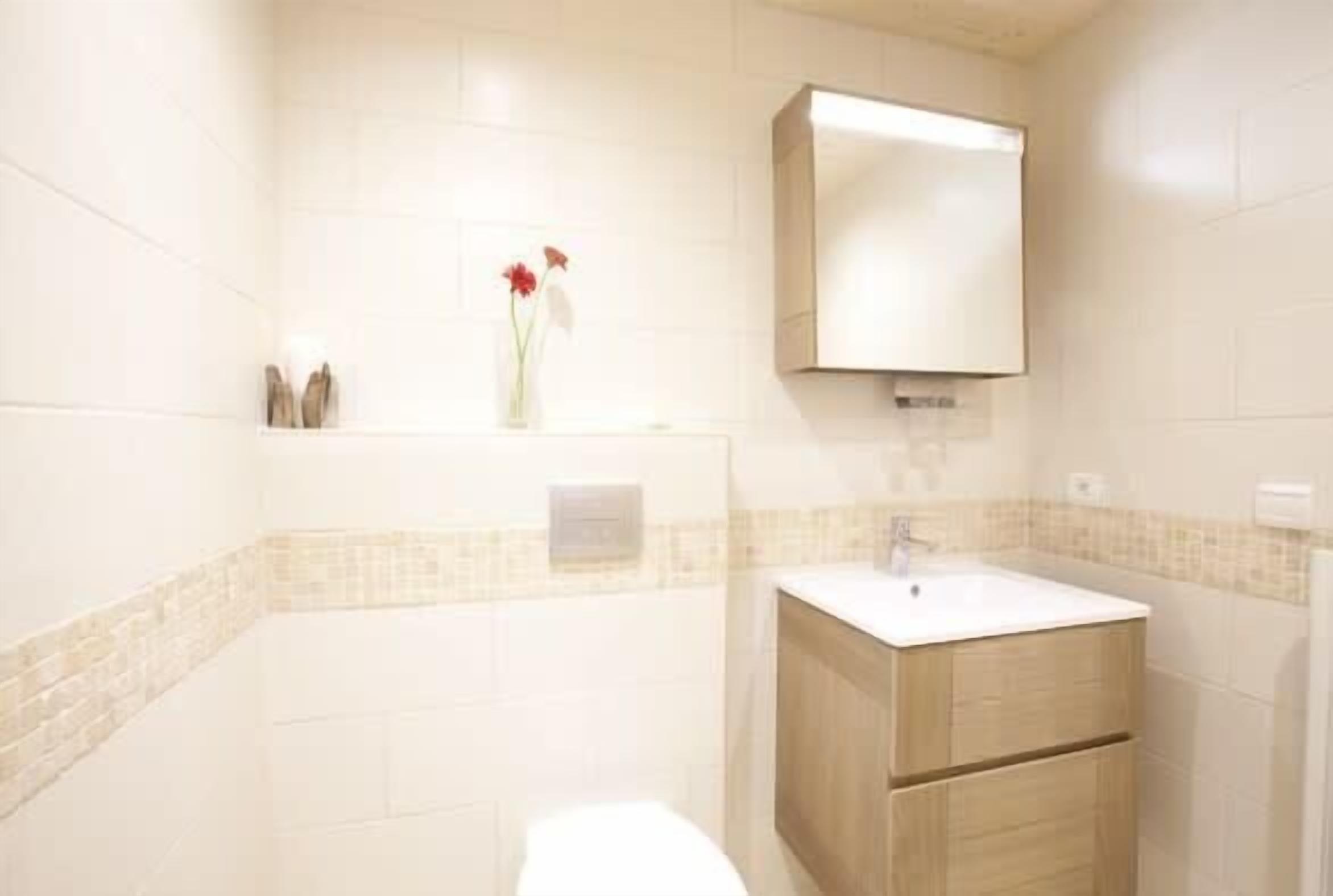 Une salle de bain avec des toilettes blanches, un meuble en bois avec un lavabo et un miroir au-dessus du lavabo.