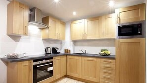 A modern kitchen with wooden cabinets, a built-in oven, a microwave, and a stainless steel range hood.