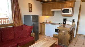 Una cocina compacta con refrigerador, microondas y horno. Hay un banco de madera y un sofá rojo.