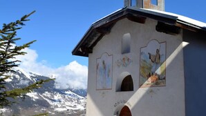 Een kerk met een klokkentoren en muurschilderingen op de gevel, gelegen tegen een besneeuwde berg.