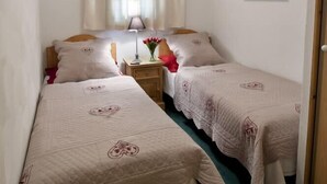 Een kleine, gezellige kamer met twee eenpersoonsbedden, een nachtkastje met een lamp en een raam met gordijnen.