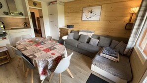 Ett mysigt vardagsrum med ett matbord, en grå soffa och en väggpanel av trä.