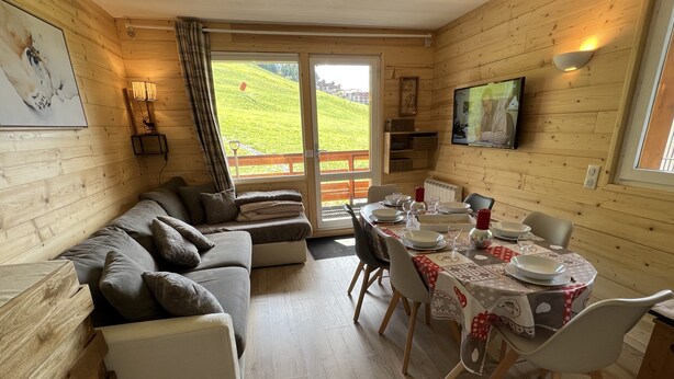 Ett mysigt rum med träinredning, en soffa, ett matbord för fyra personer och en tv på väggen.
