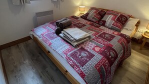 Une chambre à coucher avec un lit en bois, une couvre-lit matelassé, une fenêtre avec des rideaux, un radiateur et une lampe fixée au mur.