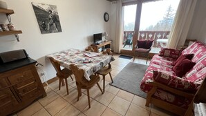 Un salon chaleureux avec une table à manger, des chaises en bois, un canapé et un balcon offrant une vue sur les arbres.