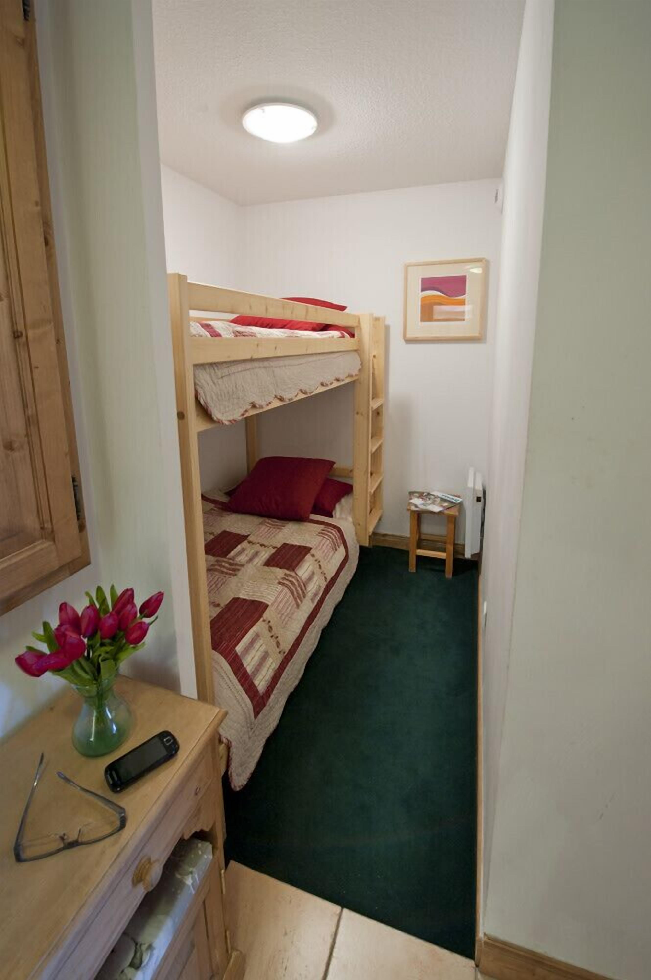 A small, cozy room with a bunk bed, a desk with a vase of flowers, and a framed picture on the wall.