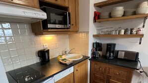 Une cuisine compacte équipée d’un four à micro-ondes, d’une machine à café et d’un grille-pain. Elle est dotée de meubles en bois et d’un pare-feu en carreaux.
