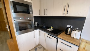 Eine kleine Küche mit weißen Schränken, einer Mikrowelle, einem Backofen und einer Kaffeemaschine.