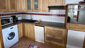Eine kompakte Küche mit Holzschränken, einer Mikrowelle, einem Geschirrspüler und einem Kühlschrank.