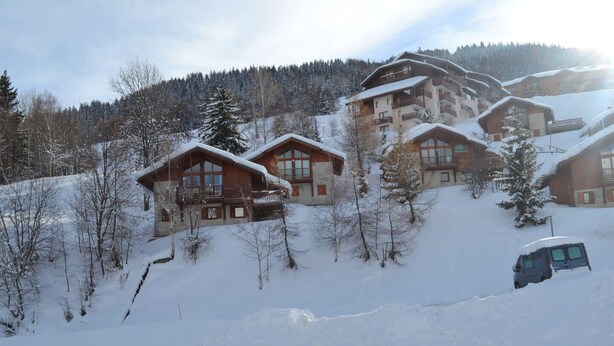 Ein mit Schnee bedecktes Chalet mit mehreren Holzhütten, einer Skiliftanlage und einem Wagen im Schnee.