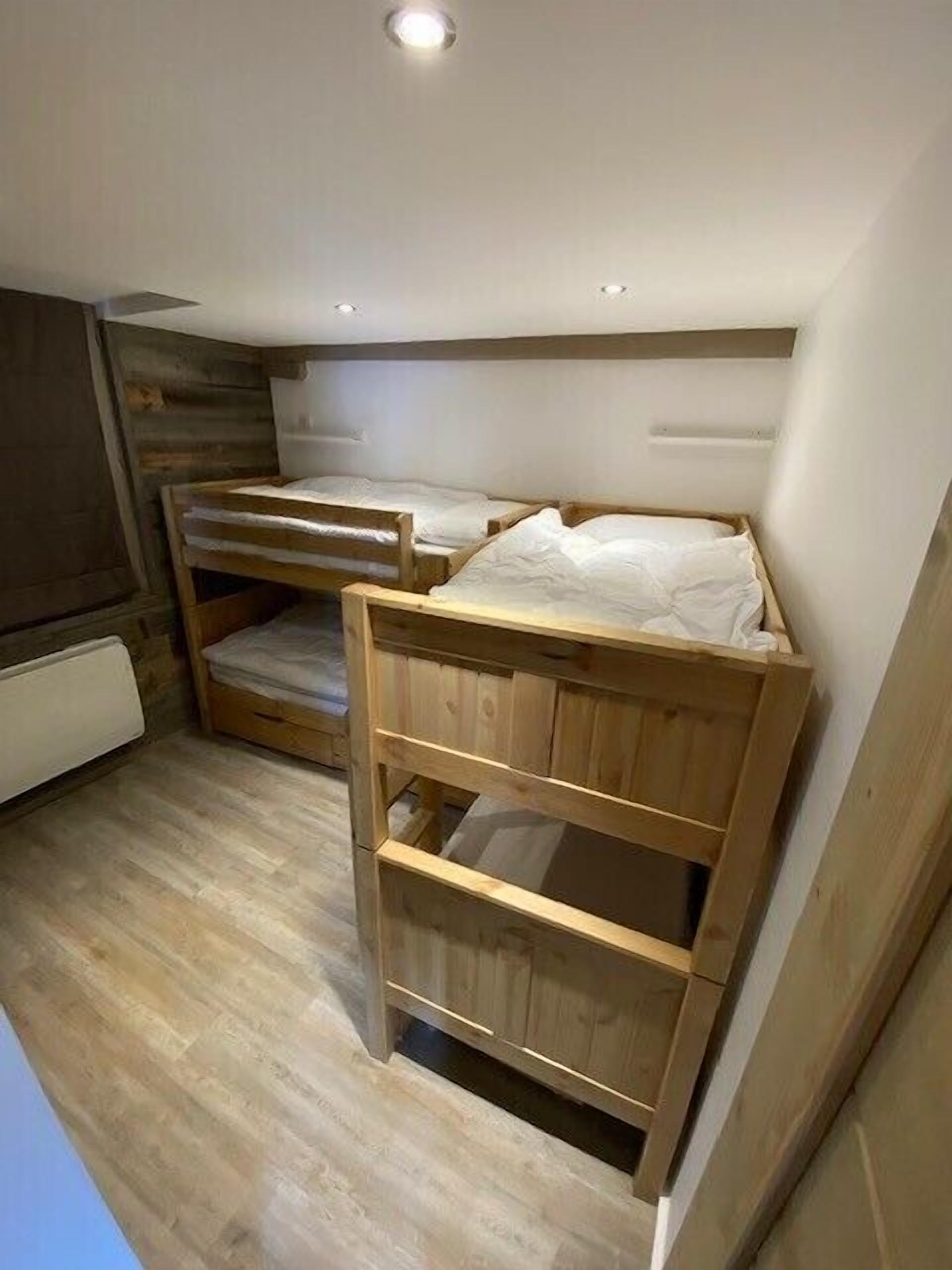 Une petite pièce compacte avec deux lits superposés, un plancher en bois et un radiateur blanc.