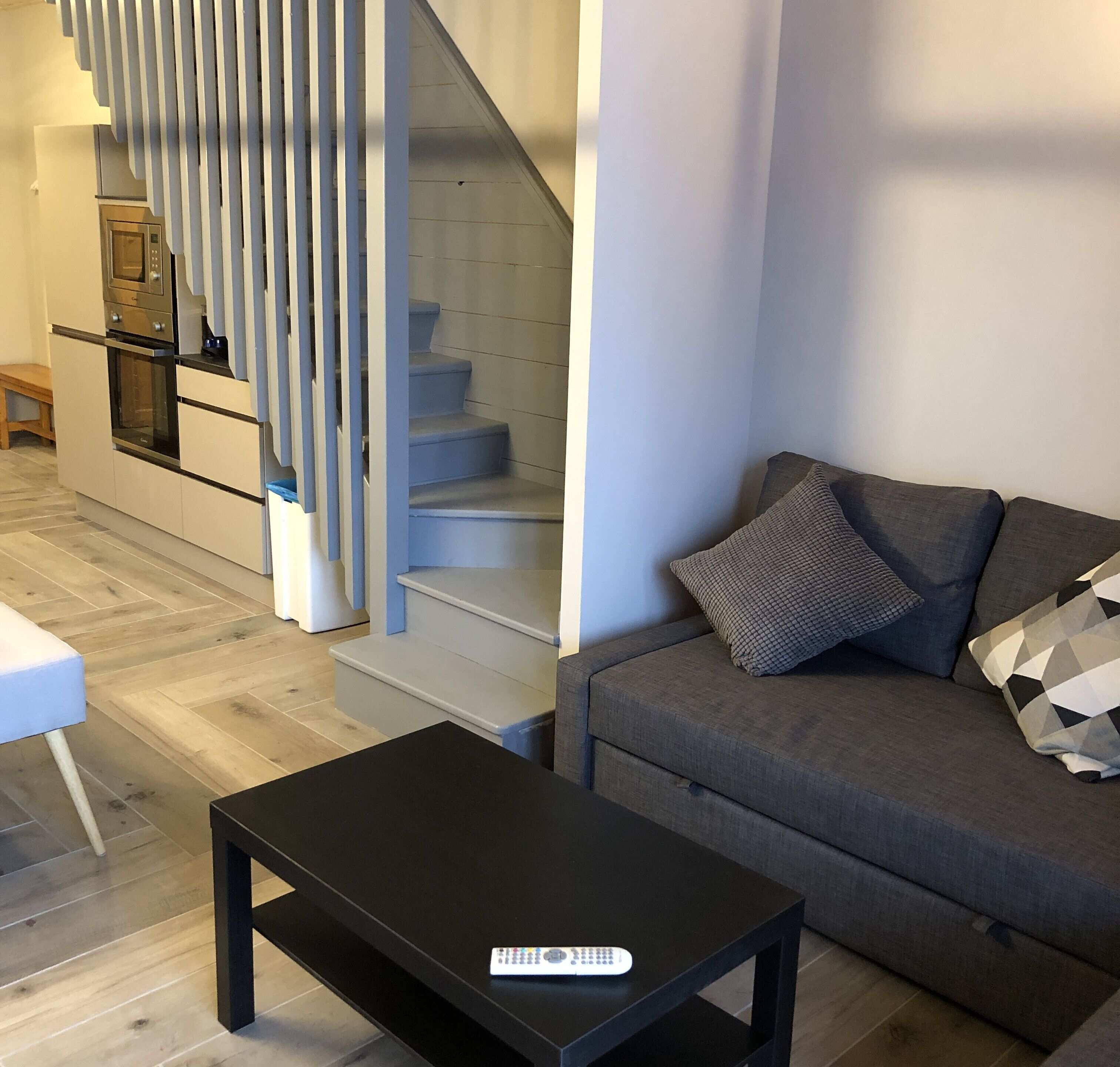 A modern living room with a grey sofa, a black coffee table, and a staircase with white railings.